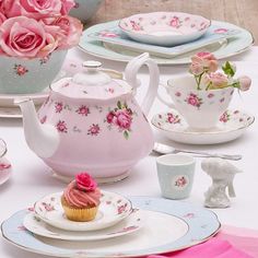 a table topped with plates and cups filled with pink flowers next to cupcakes