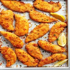 chicken tenders with lemon wedges on a baking sheet, ready to be cooked