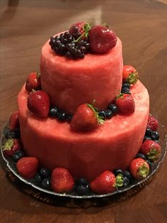 a three tiered cake with berries and blueberries on the top is sitting on a wooden table