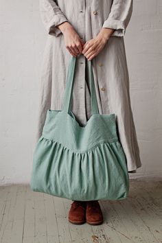 a woman is holding a green bag in her hands and standing on the floor with white walls behind her