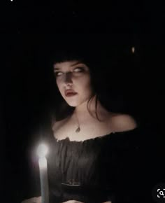 a woman holding a lit candle in her hand and looking at the camera with an evil look on her face