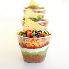 three cups filled with different types of food on top of a white tablecloth and red background