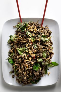 a white plate topped with noodles and veggies next to two red chopsticks