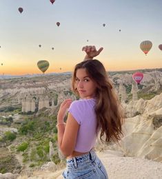 a woman standing on top of a hill with hot air balloons flying in the sky