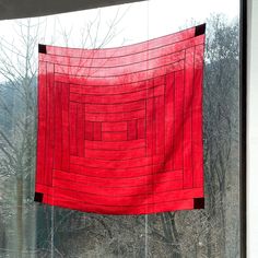 a red piece of cloth hanging on a window sill in front of some trees