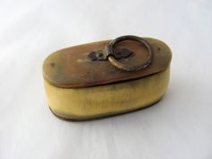 an old brass box with a ring on the lid sitting on a white tablecloth