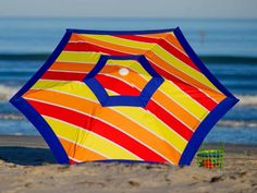 a colorful umbrella sitting on top of a sandy beach next to the ocean with waves in the background