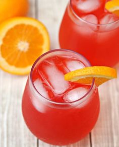 two glasses filled with red liquid and garnished with an orange slice on the rim