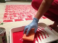 a person in blue gloves is spreading red paint on a piece of bread with a sponge