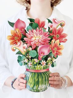 a woman holding a vase filled with lots of pink and orange flowers in her hands