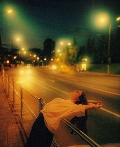 a woman leaning against a rail on the side of a road at night with her arms stretched out