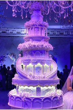 a bride and groom standing in front of a large wedding cake with purple lights on it