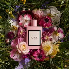 a bottle of gucci perfume surrounded by flowers and greenery on the ground in front of an array of wildflowers