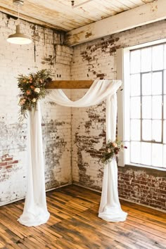 the wedding arch is decorated with greenery and white draping, along with flowers