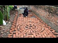 a man kneeling down next to a brick wall with an intricate design on the ground