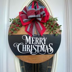 a merry christmas sign hanging on the front door with red and white bows, greenery and holly