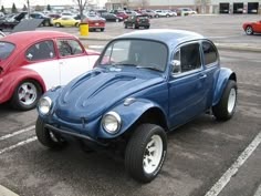 a blue beetle parked in a parking lot next to another red one and white one