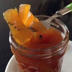 a jar filled with liquid and sliced fruit on top of a white plate next to a spoon