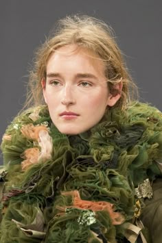 a woman with long hair wearing a green jacket and scarf over her shoulders is looking at the camera