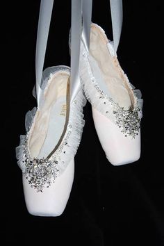 two pairs of white ballet shoes with bows on the bottom and silver beading around the toes