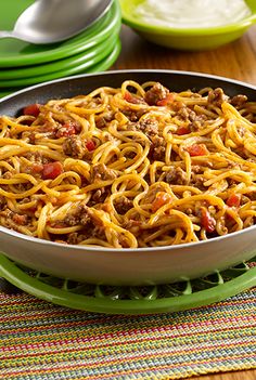 a skillet filled with spaghetti and meat sitting on top of a table next to green plates