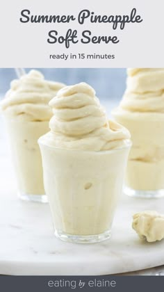 three small cups filled with whipped cream on top of a white marble plate next to two spoons