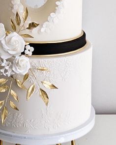 a three tiered white wedding cake with gold leaves and flowers