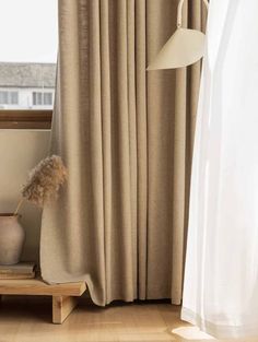 a white vase sitting on top of a wooden shelf next to a window covered in curtains