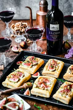 some food is laying out on a tray next to wine glasses and other foods that are sitting on the table