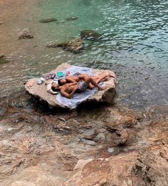 two people are laying on a rock in the water