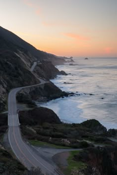 an empty road on the side of a cliff next to the ocean at sunset or sunrise