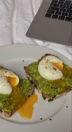 two pieces of toast with avocado and an egg on top, next to a laptop