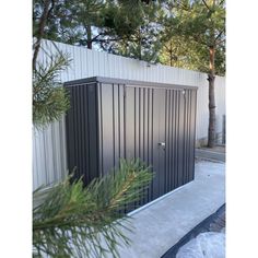 an outdoor toilet in front of a white fence and pine tree with snow on the ground