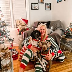 a woman sitting on the floor with two dogs in her lap and christmas decorations around her