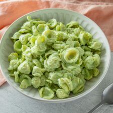 a white bowl filled with green pasta on top of a table next to utensils