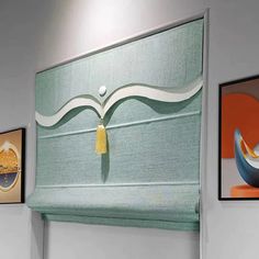 three paintings hang on the wall above a window with roller shades in an office setting