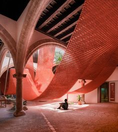 a person sitting on the ground in front of a building with red mesh covering it