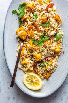 a white plate topped with rice, cauliflower and lemon wedges next to a fork