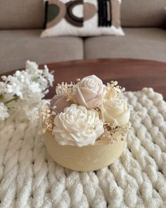 a table topped with white flowers on top of a knitted blanket next to a couch