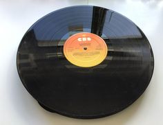 a black record with yellow label sitting on top of a white table next to a wall