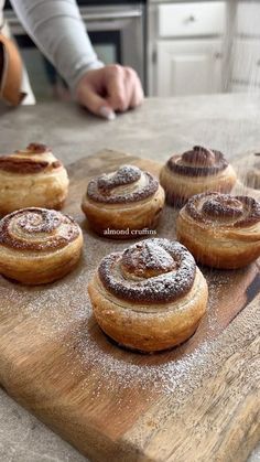 cinnamon rolls on a wooden cutting board being sprinkled with powdered sugar