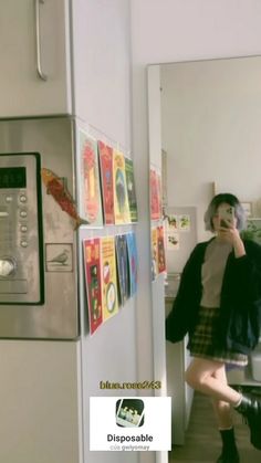 a woman standing in front of a refrigerator talking on a cell phone while holding a camera