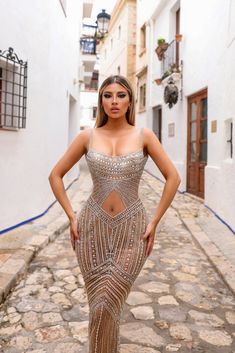 a woman in a gold dress standing on a cobblestone street with her hands on her hips