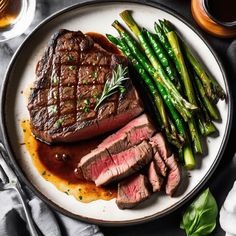 steak, asparagus and sauce on a plate with silverware next to it