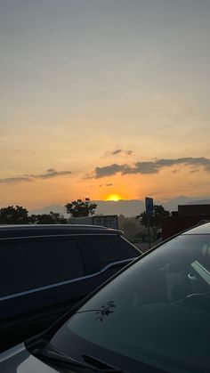 the sun is setting behind some cars on the road in front of another car with its hood up