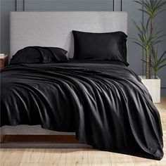 a bed with black sheets and pillows in a room next to a potted plant