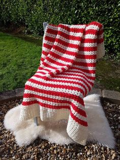 a red and white striped blanket sitting on top of a pile of rocks next to a bush