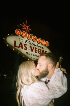 a man and woman kissing in front of the welcome to fabulous las vegas sign at night