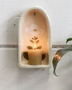 a candle that is sitting in a white wall mounted holder with a flower on it