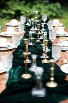 a long table is set with white plates and silver candlesticks on green velvet